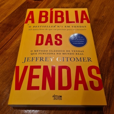 Livro A Bíblia das Vendas de capa amarela com texto vermelho e azul sobre madeira