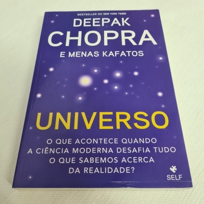 Capa de livro roxa com título UNIVERSO e texto em branco e amarelo, sobre fundo de tecido branco.