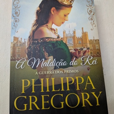 Capa de livro com mulher de vestido verde e coroa dourada segurando um cálice em frente a castelo