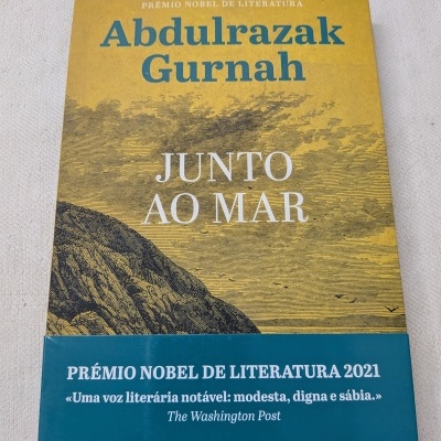 Capa do livro Junto ao Mar de Abdulrazak Gurnah com faixa azul promocional.