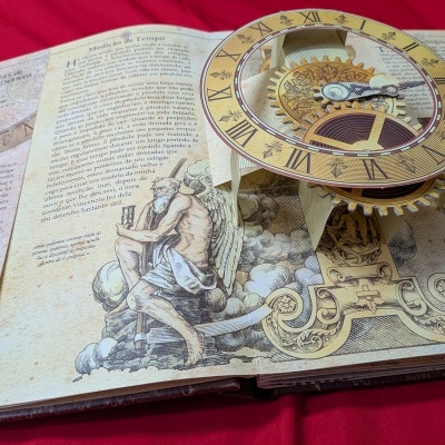 Livro pop-up com ilustração e texto sobre medição do tempo e relógio mecânico em 3D.