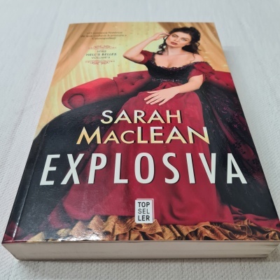 Capa do livro Explosiva de Sarah MacLean com mulher em vestido vermelho e preto, sentada num sofá vermelho