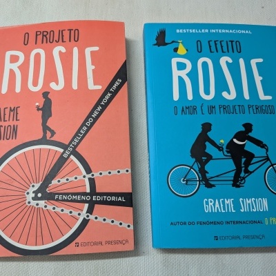 Dois livros coloridos titulados O PROJETO ROSIE e O EFEITO ROSIE sobre uma superfície clara.