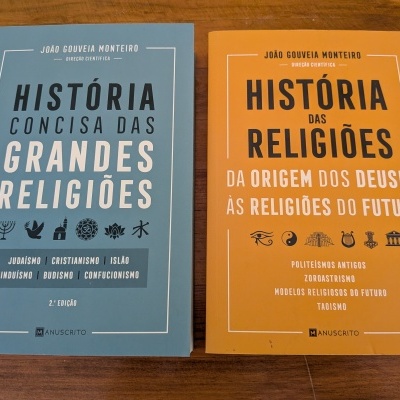 Dois livros sobre religiões com capas azul clara e laranja em superfície de madeira
