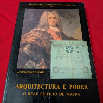 Capa de livro preta com retrato e planta arquitetónica em cima de tecido vermelho