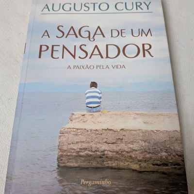 Capa de livro de romance A SAGA DE UM PENSADOR de Augusto Cury com imagem de uma pessoa sentada num cais de pedra à beira-mar