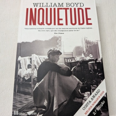 Capa do livro INQUIETUDE de William Boyd com imagem preto e branca de uma pessoa sentada no chão e vários textos promocionais.