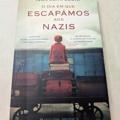 Capa de livro com criança vestida de vermelho sentada em malas num carrinho de bagagem