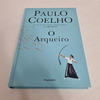 Capa de livro azul com título 'O Arqueiro' de Paulo Coelho e ilustração de arqueira