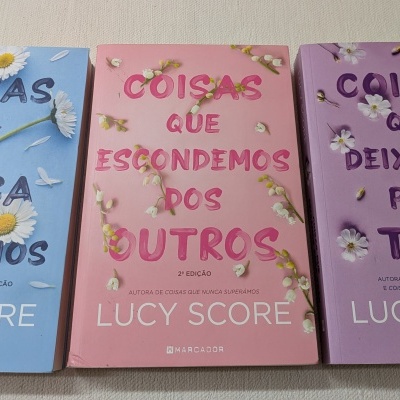 Três livros de capa mole em azul, rosa e lilás com flores e texto em português