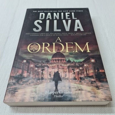Capa do livro 'A Ordem' de Daniel Silva com imagem noturna de rua e pessoa a caminhar.