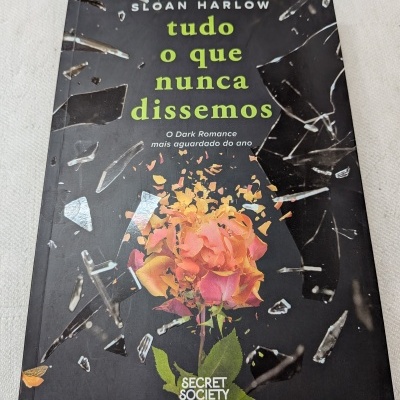 Capa de livro preto com rosa desintegrando-se e fragmentos de vidro.
