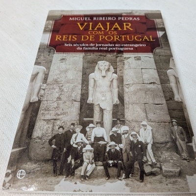 Livro Viajar com os Reis de Portugal com fotografia antiga de pessoas junto a estátuas egípcias.