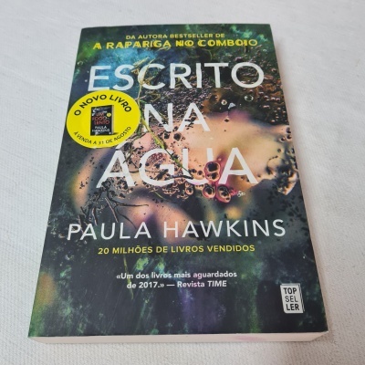 Capa de livro 'Escrito na Água' de Paula Hawkins com fundo de bolhas e selo amarelo