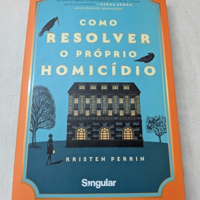 Capa de livro azul com bordas laranja e ilustração de edifício, corvos e figura feminina