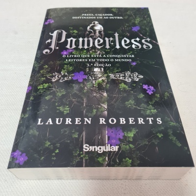 Capa do livro Powerless de Lauren Roberts com decoração de flores roxas e crânio.