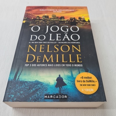 Capa do livro 'O Jogo do Leão' de Nelson DeMille com design urbano e texto promocional.