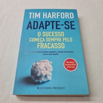 Livro 'Adapte-se' de Tim Harford com capa azul e selo vermelho