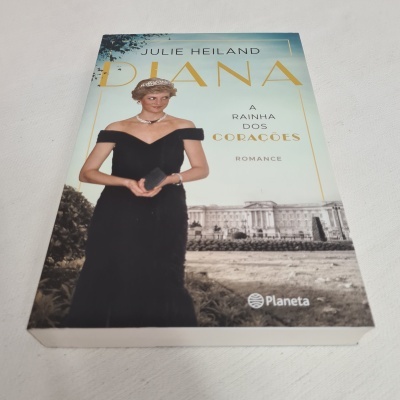 Capa do livro 'DIANA A RAINHA DOS CORAÇÕES' com imagem de mulher em vestido preto e tiara, fundo de edifício histórico