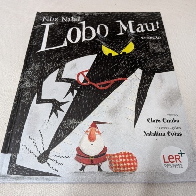 Capa de livro infantil 'Feliz Natal Lobo Mau!' com lobo preto e personagem vermelho com saco xadrez