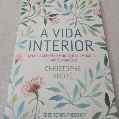 Capa de livro com flores e folhas verdes e texto em azul, vermelho e dourado