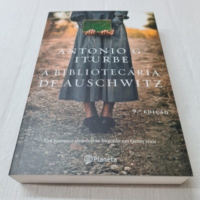 Capa de livro com mulher de vestido listrado segurando livro verde em caminho de terra