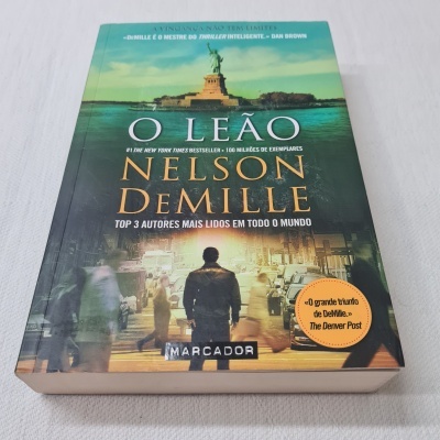 Capa do livro 'O LEÃO' de Nelson DeMille com imagem da estátua da liberdade e figura masculina.