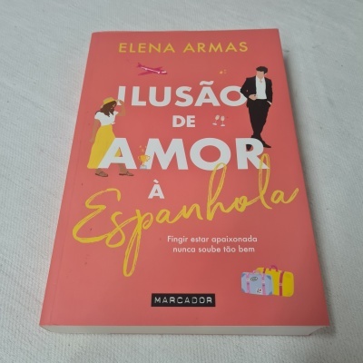 Capa de livro cor de rosa com título Ilusão de Amor à Espanhola e ilustrações de personagens e malas