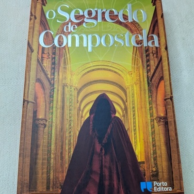 Capa do livro o Segredo de Compostela mostrando figura com capa escura e interior com arcos iluminados