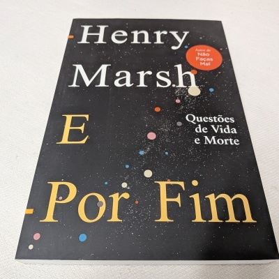 Livro preto com pontos coloridos e texto em branco e amarelo sobre superfície branca