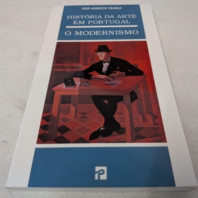 Capa do livro 'História da Arte em Portugal: O Modernismo' com ilustração de um homem sentado numa mesa.