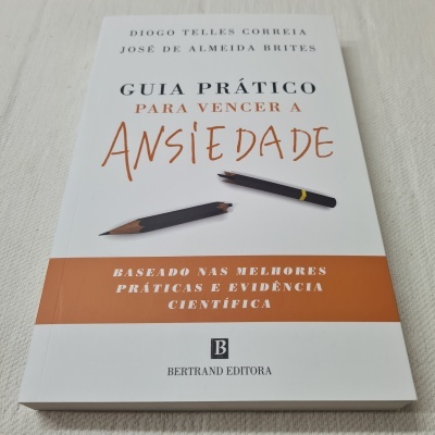 Livro Guia Prático para Vencer a Ansiedade com capa branca e detalhes em laranja e dois lápis partidos na frente.