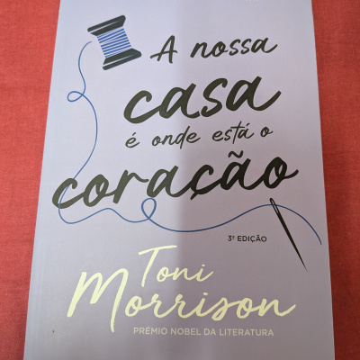 Capa lilás de livro A nossa casa é onde está o coração de Toni Morrison com ilustração de carretel e agulha