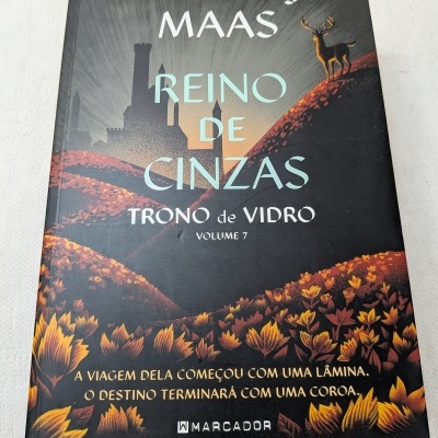 Capa de livro Reino de Cinzas com castelo e cervo em colinas floridas