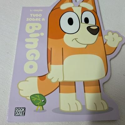 Capa de livro infantil com personagem de cão cor de laranja e branco, texto TUDO SOBRE A Bingo e logótipo BOOK SMILE.