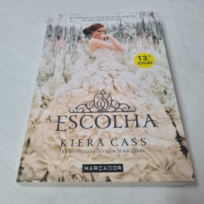 Livro 'A ESCOLHA' de Kiera Cass com capa ilustrada de mulher com vestido branco e detalhes florais