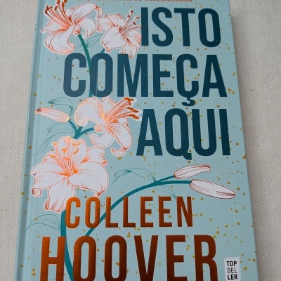 Livro ISTO COMEÇA AQUI de Colleen Hoover com capa azul, flores e texto em laranja e azul