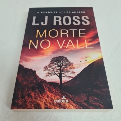 Capa do livro 'MORTE NO VALE' de LJ ROSS com paisagem de montanha e árvore ao pôr do sol