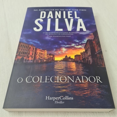 Capa do livro 'O Colecionador' de Daniel Silva com imagem de canal ao pôr do sol.