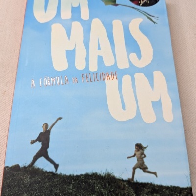 Capa do livro Um Mais Um de Jojo Moyes com fundo azul e pessoas a correr num campo verde.