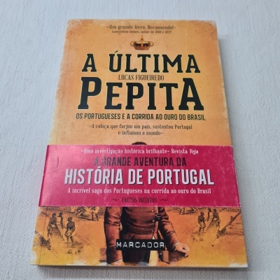 Livro 'A Última Pepita' de Lucas Figueiredo com capa amarela e vermelha sobre superfície cinzenta