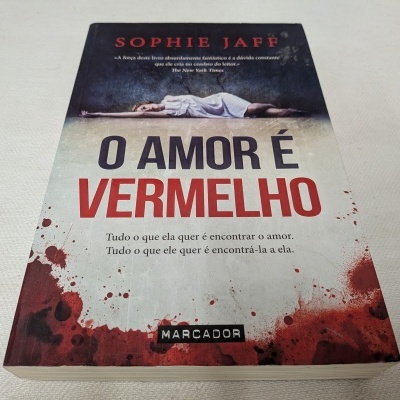 Livro 'O AMOR É VERMELHO' com capa em branco e vermelho e imagem de mulher deitada
