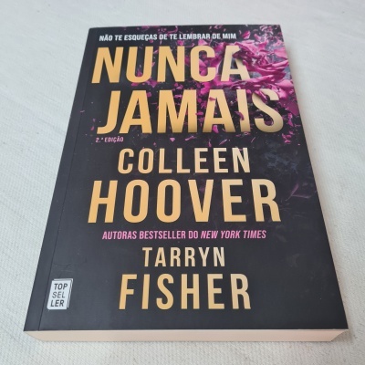 Livro 'NUNCA JAMAIS' com capa preta e letras douradas e rosas sobre fundo branco