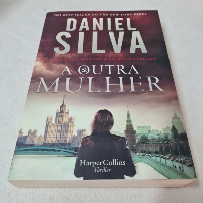 Capa do livro 'A Outra Mulher' de Daniel Silva com mulher de costas e paisagem urbana ao fundo