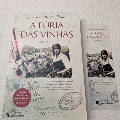 Livro 'A FÚRIA DAS VINHAS' com marcador de livro, ambos com imagem de vinha e pessoas em tons sépia.