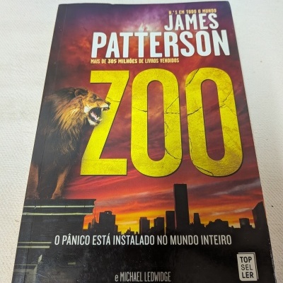 Livro ZOO de James Patterson com ilustração de leão e cidade ao entardecer
