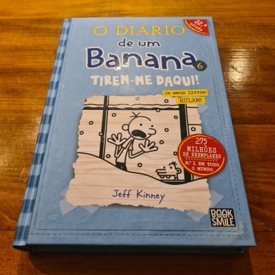 Livro O Diário de um Banana 6 Tirem-me Daqui em capa azul sobre mesa de madeira