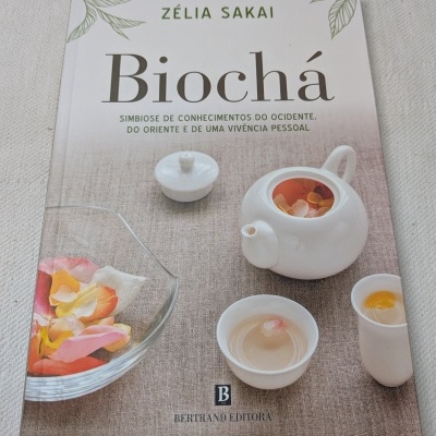 Capa do livro Biochá de Zélia Sakai com bule e chávena branca e pétalas de flores em superfície bege