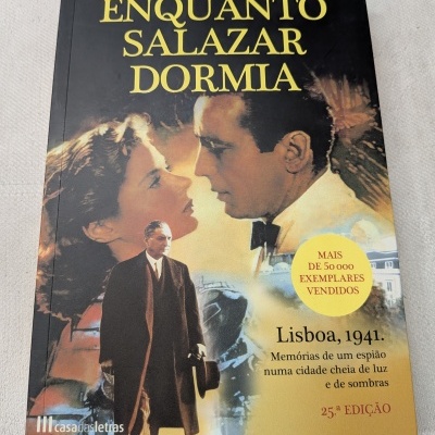Capa livro Enquanto Salazar Dormia de Domingos Amaral com imagens e texto informativo.