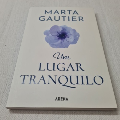 Livro 'Um Lugar Tranquilo' com capa branca e flor azul